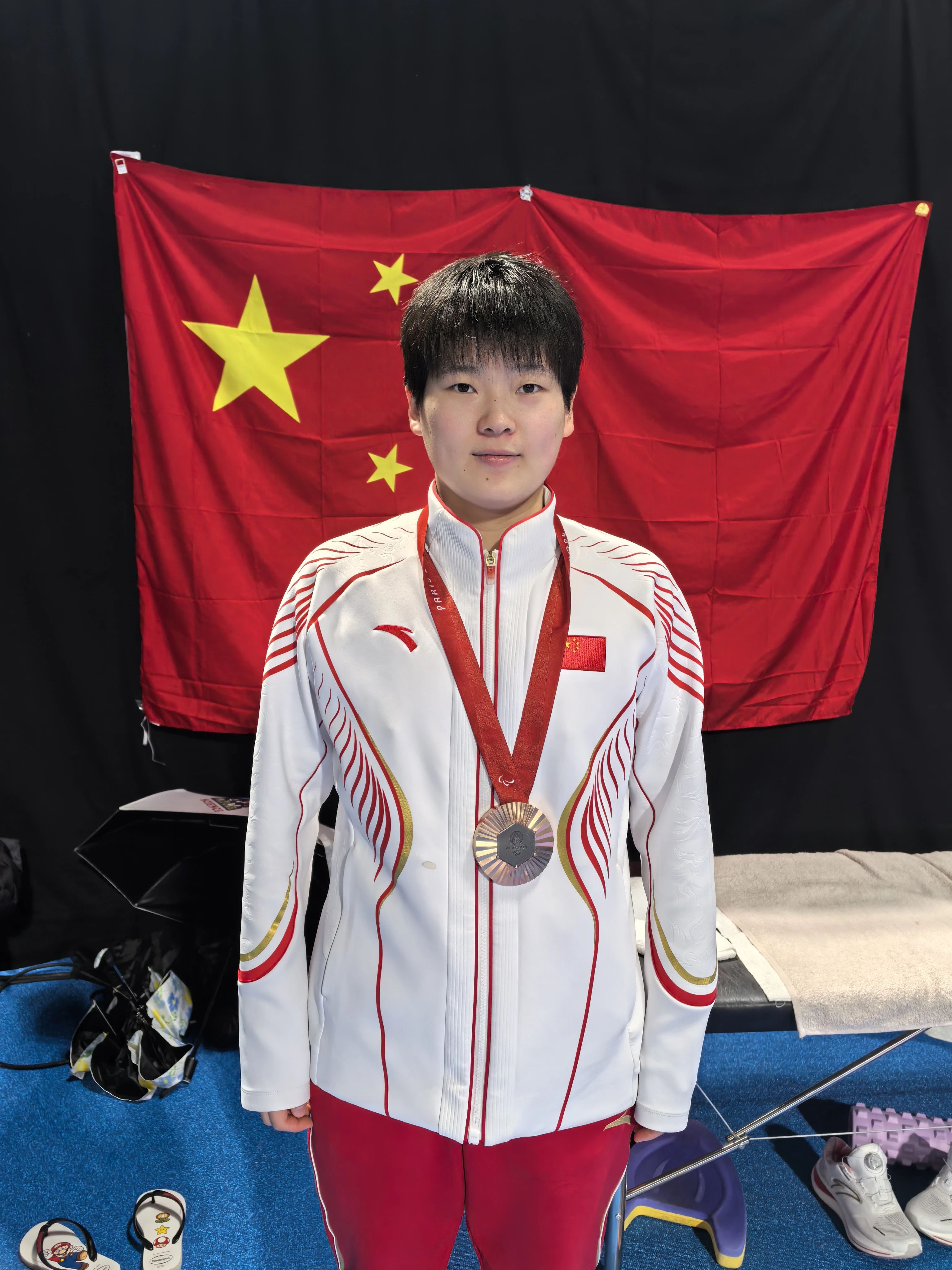 图为残疾人游泳运动员郑杰桐在获得一枚宝贵的铜牌后与国旗合影